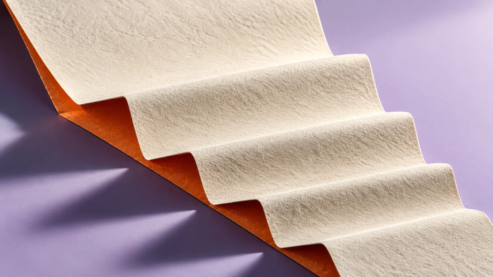 Cream paper folded into descending steps with a burnt-orange underside over a lavender surface