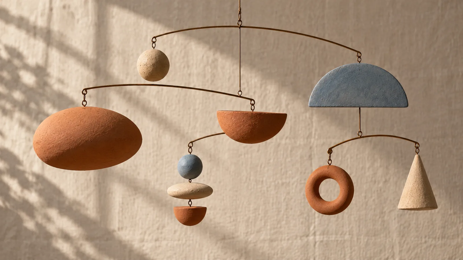 Several terracotta shapes balance on a hanging mobile against a linen wall